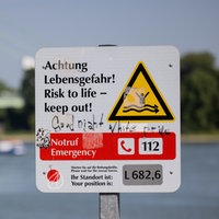 Ein Hinweisschild mit der Aufschrift "Achtung Lebensgefahr" weist am Rhein in Rodenkirchen auf die Gefahren beim Schwimmen in dem Fluss hin.