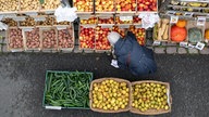 Eine ältere Person sucht ein paar Äpfel aus Holzkisten