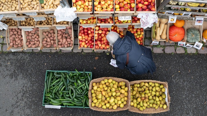 Eine ältere Person sucht ein paar Äpfel aus Holzkisten