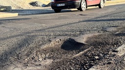 Großes Schlagloch auf einer Straße in Lüdenscheid mit einem Auto in Hintergrund