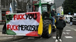 Mann steht neben einem Traktor mit einem Plakat mit der Aufschrift „UE-Fuck you / Fuck Mercosur”