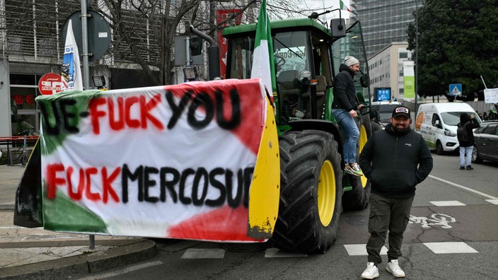 Mann steht neben einem Traktor mit einem Plakat mit der Aufschrift „UE-Fuck you / Fuck Mercosur”