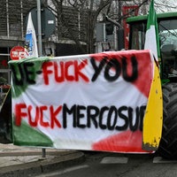 Mann steht neben einem Traktor mit einem Plakat mit der Aufschrift „UE-Fuck you / Fuck Mercosur”