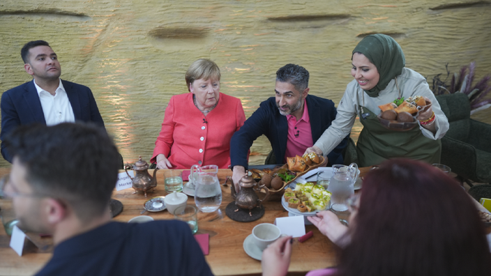 Angela Merkel sitzt am Essenstisch des syrischen Restaurants und unterhält sich 