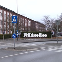 Außenansicht des Miele-Werks mit einem Schild mit dem Miele Schriftzug davor