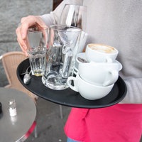 Eine kellnernde Person trägt ein Tablett mit benutztem Geschirr