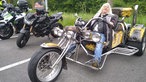 Ein Mann mit langen grauen Haaren sitzt auf einem großen buntem Motorrad mit drei Rädern.