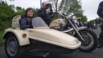 Ein Junge sitzt in einem beigen Beiwagen von einem altem Motorrad.