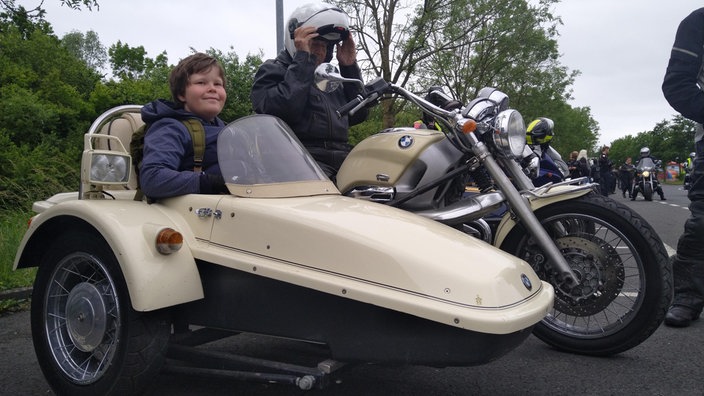 Ein Junge sitzt in einem beigen Beiwagen von einem altem Motorrad.