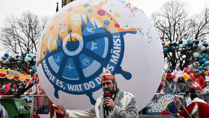 Das Motto für die nächste Session "·Morje es, wat do drus mähs!" steht auf einem Ball, welches vom Zugleiter des Kölner Rosenmontagszug, Marc Michelske, präsentiert wird. 