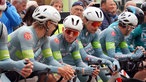 Vor dem Start lehnen die Profis in hellblauen Trikots, mit weißen Helmen und rosa Sonnenbrillen entspannt auf dem Lenker ihrer Räder.
