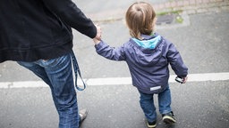 Eine Mutter hält ihren Sohn an der Hand und kreuzen die Straße