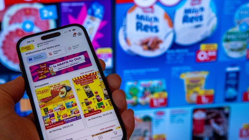 Ein Smartphone mit der Rabatt- und Coupon-App des Supermarkts Netto ist vor Werbeanzeigen zu sehen
