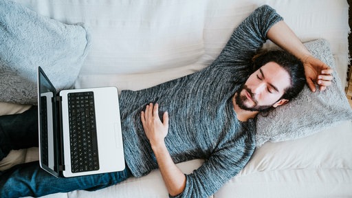 Mann schläft mit seinem Laptop auf dem Schoß auf dem Sofa