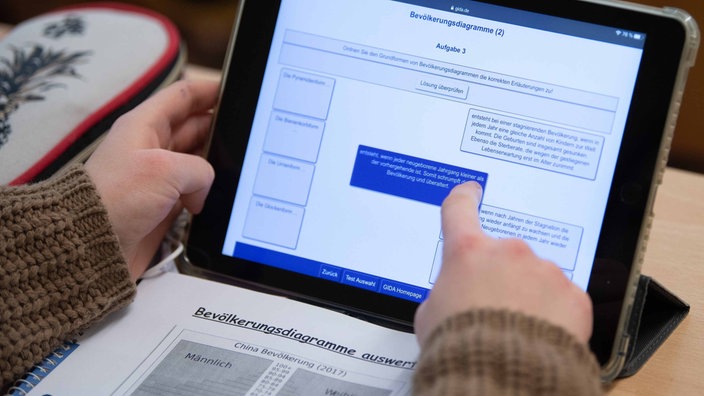 Eine Schülerin arbeitet an einem Tablet, daneben liegt ein Block und ein Stiftemäppchen 