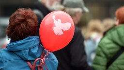 Ein Luftballon mit einer Friedenstaube ist am Rucksack einer Frau befestigt
