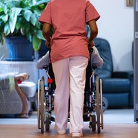Eine Bewohnerin eines Pflegeheims wird von einer Pflegerin einen Gang entlang geschoben