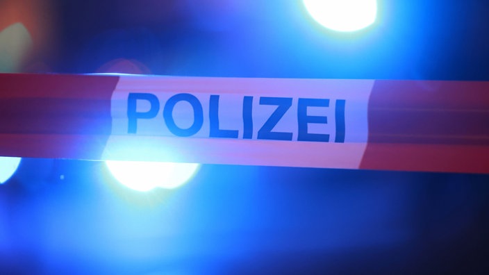 Blaulichter leuchten hinter einem Absperrband der Polizei