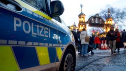 Ein Polizeiauto steht neben den Absperrungen gegen Anschläge mit Fahrzeugen am Kölner Weihnachtsmarkt in Heumarkt