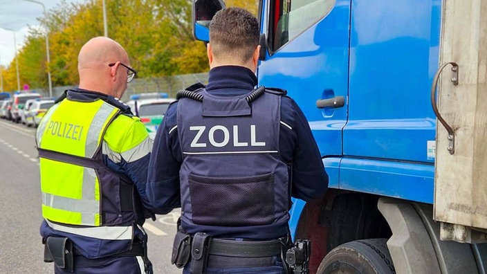 Ein Zoll- und ein Polizeibeamter vor einem LKW