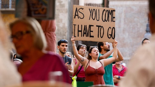 Eine Frau hält ein Schild mit der Aufschrift "As you come - I have to go" bei der Demo gegen Massentourismus hoch