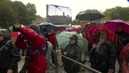 Besucher des Bürgerfests auf der Rahmedetalbrücke stehen mit Regenschirmen vor der Bühne.