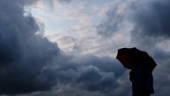 Ein Mann geht mit einem Regenschirm vor aufziehenden dunklen Wolken spazieren.
