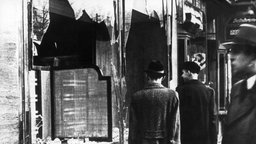 Passanten vor einer zerstörten Fensterfront eines jüdischen Geschäfts.