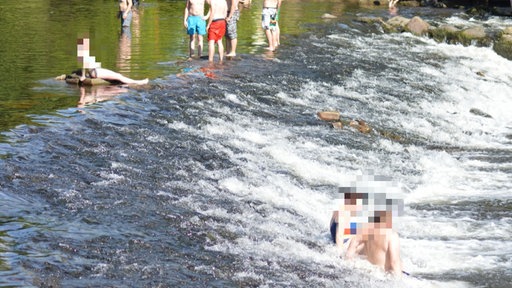 man sieht mehrere Menschen, die gepixelt wurden, die in der Wupper direkt an den Wupperkotten baden