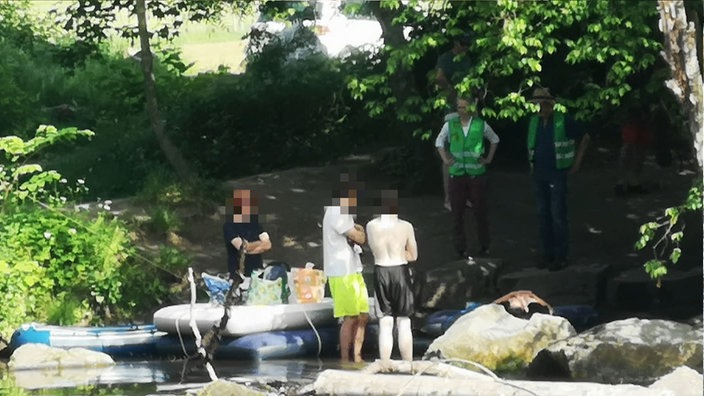 Man sieht Menschen mit Schlauchboot am Ufer der Wupper, direkt neben den Wupperkotten. Vor ihnen stehen Aufpasser in grüner Warnweste.