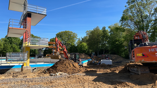 Zwei Bagger und eine Menge an Erdehaufen stehen und den 10 Meter Turm, der sich in Richtung des neuen Beckens richtet. 