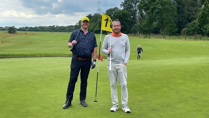 Zwei Männer stehen mit Golfschlägern auf einem Golfplatz vor 