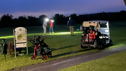 Menschen spielen Golf mit Flutlichtern nach Einbruch der Dämmerung