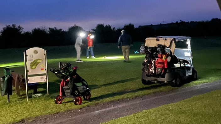 Menschen spielen Golf mit Flutlichtern nach Einbruch der Dämmerung