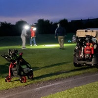 Menschen spielen Golf mit Flutlichtern nach Einbruch der Dämmerung