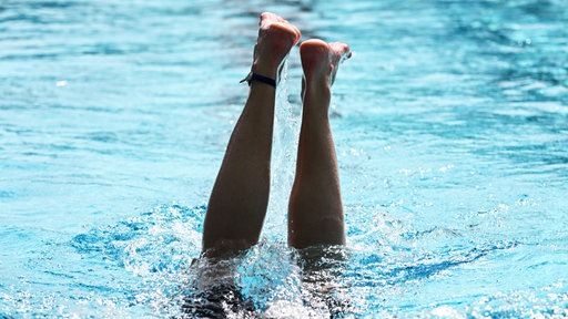 Aus einem Schwimmbecken ragen zwei Beine in die Höhe nach einem Kopfsprung ins Wasser