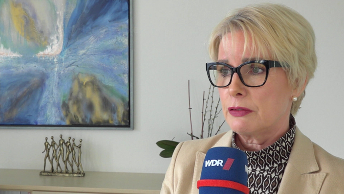 Claudia Hardenacke trägt eine schwarze Brille, hat kurze blonde Haare und wir mit einem Mikrofon interviewt. 