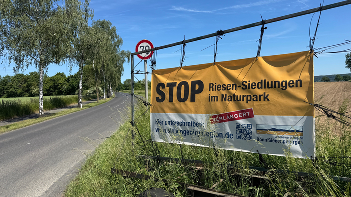 Am Straßenrand einer Landstrasse hängt ein Plakat, dass für eine Petition zum Schutze des Naturparks des Siebengebirges wirbt.
