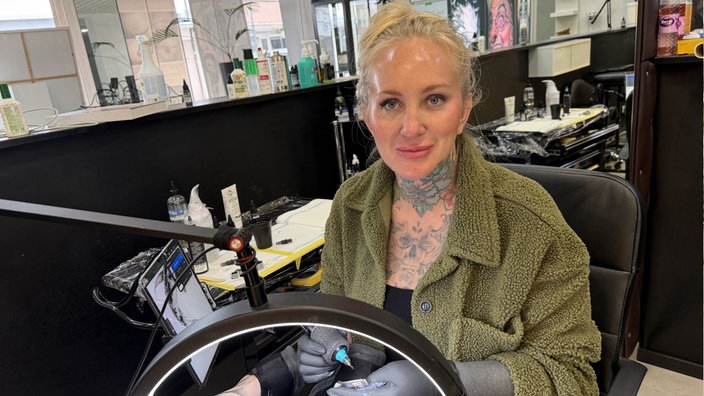 Eine Frau mit Tattoos auf der Brust mit Tattowerkzeug in der Hand an ihrem Arbeitsplatz