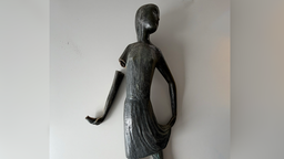 Eine Bronzefigur liegt auf einem Tisch, der rechte Arm der Figur ist abgebrochen und liegt daneben.