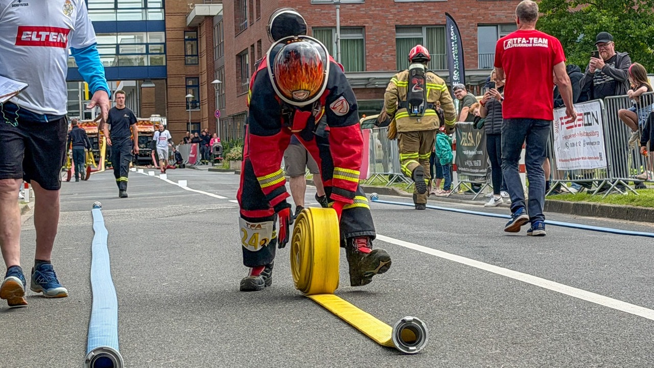 Ein Feuerwehrmann rollt in Uniform einen gelben Schlauch auf