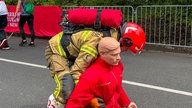 Eine Feuerwehrfrau zieht eine menschensgroße Übungspuppe auf der Wettkampfstrecke