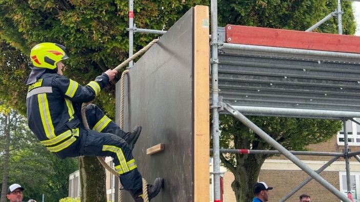 Ein Feuerwehrmann klettert an einem Seil eine Kletterwand hoch