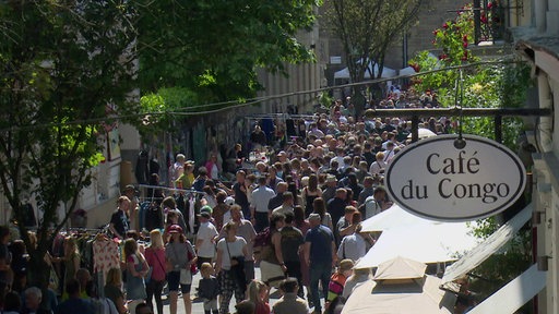 Menschen auf der Luisenstraße bei sonnigem Wetter, Rechts im Bild Schild Café du Congo