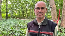 Stadtförster Stefan Jeschke steht vor einem weiß-roten Absperrband im Wald.