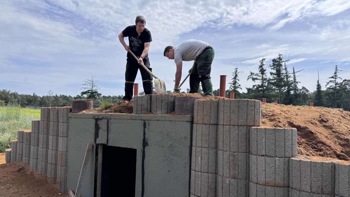 Zwei Männer bauen eine Höhle und schauflen den Dach der Höhle zu