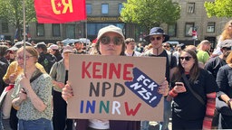 Die Demonstrantin Katharina Pfeiffer hält ein Schild, auf dem „Keine NPD in NRW“ steht. Im Hintergrund stehen weitere demonstrierende Menschen.