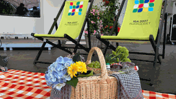 Ein Picknick Korb steht auf einer Picknickdecke und hinter ihm zwei Stühle mit dem Logo der IGA darauf