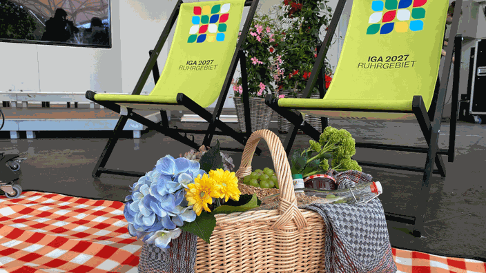 Ein Picknick Korb steht auf einer Picknickdecke und hinter ihm zwei Stühle mit dem Logo der IGA darauf