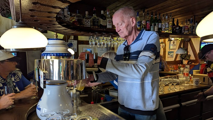 Ulf Timmermann, ein älterer Mann, steht hinter einer Theke und zapft ein Bier.
